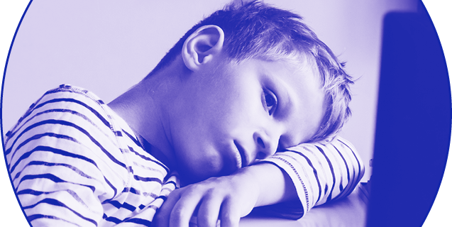 Distracted young boy, head resting on arm, aimlessly looking at a computer screen